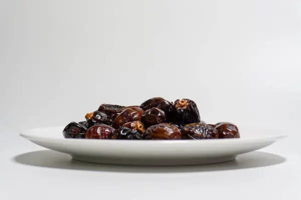 Beyaz arka planda kurumuş tarihler. Birinci kalite meyve tabakta izole edilir. Beyaz arkaplan ile tarih meyvesi.