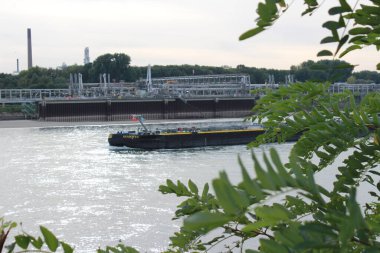 Rhine nehrinde kargo gemisi. Arka planda ham petrol işleme tesisi var.