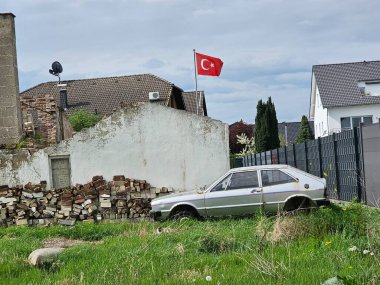Schrottauto (Auto) auf einem ungepflegtem Gelaende und baufaelligem Gebaeude, im Hintergrund die tuerkische Flagge clipart