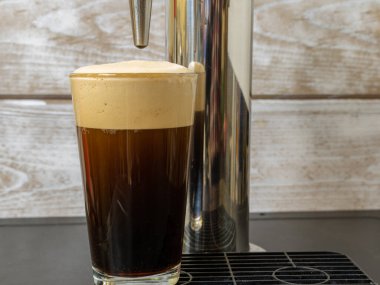 Nitro Cold Brew kahvesi, temiz bir bardağa dökülüyor. İçinde nitrojen kabarcıkları ve fıçı kahve makinesinde pürüzsüz bir doku var..