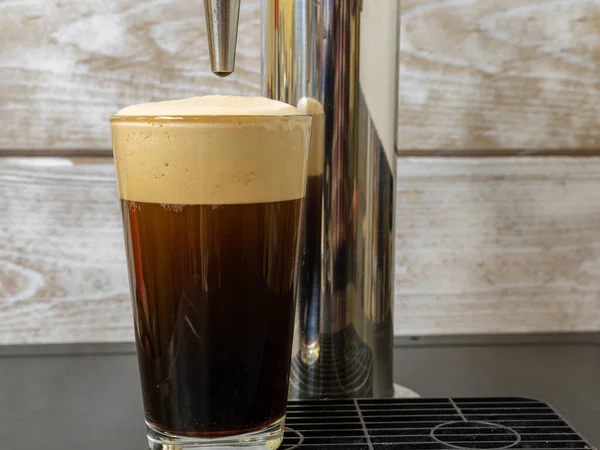 Nitro Cold Brew coffee pouring into a clear glass with fine nitrogen bubbles and a smooth texture on a keg coffee dispenser.