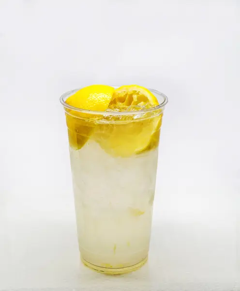 Fresh squeezed lemonade in a clear cup with lemon slices and ice cubes isolated on a white background..