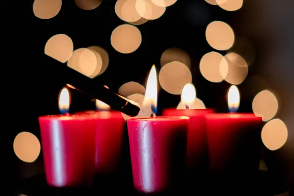 Beş kırmızı mumun gece karanlığında çözülmüş bir Noel ağacının önünde çakmakla yakıldığı yakın plan fotoğraf.