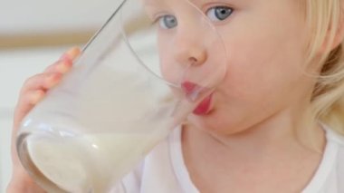 Sarı saçlı neşeli çocuk bir bardak süt içiyor. 