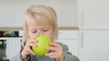 Şüpheci görünüşlü, komik sarışın, mutfakta yeşil elma tutan küçük bir çocuk. 
