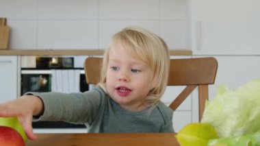 Sevimli küçük bir çocuk, mutfakta neşeli bir kız, kırmızı elmayı alıyor ve ısırıyor, video.