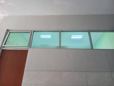 Kapıdaki üst cam pencereler, temiz fayanslı iç döşemede floresan ışığı gösteriyor.