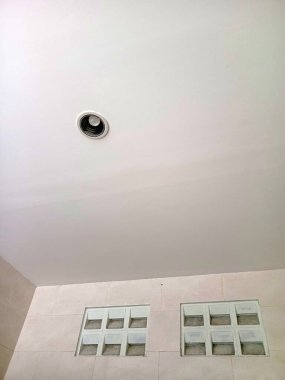 Temiz, minimalist bir tavan, aralıklı aydınlatma armatürü ve fayanslı bir duvarda iki set cam bloklama penceresi, modern iç tasarımı sergiliyor.