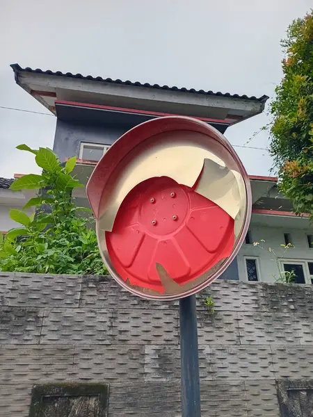 Yansıtıcı yüzeyi kötü soyulmuş ve hasar görmüş kırmızı bir dışbükey yol aynası.