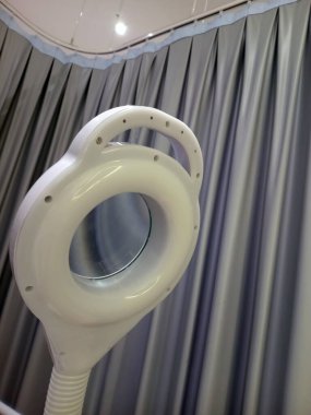 Tıbbi veya güzellik ortamında gri perdelere karşı beyaz bir büyüteç yakın çekim