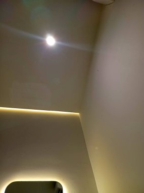 Kenarında lamba armatürü ve çevre aydınlatması olan bir tavan manzarası. Duvar açık bir renge boyanarak modern ve minimalist bir atmosfer yaratıyor..