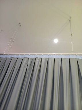 Açık mavi süslemeli, tavandan sarkan gri perdelerin yakın görüntüsü. Arka plan yumuşak, dağınık bir ışık kaynağına sahip, sakin bir atmosfer yaratıyor..