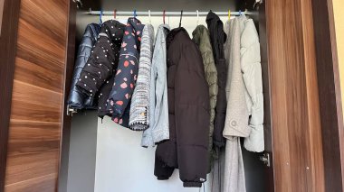 Kışlık ceketler ahşap bir gardıroptaki renkli askılarda asılı.