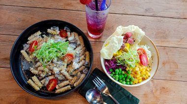 Mantarlı makarna, sebze salatası ve restoran masasında bir bardak meyve suyu.
