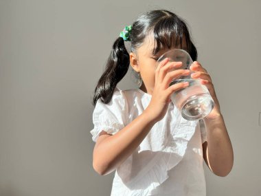 Asyalı bir kız bir bardak saf temiz maden suyu içiyor ve her gün sağlıklı bir yaşam tarzı öneriyor. Havalandırılmış su ya da meşrubat içmeyi bırak, su çocuk için iyidir..