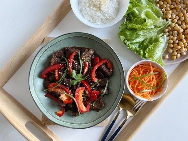 Asya yemekleri: Kırmızı biberli biftek Teriyaki ve bir tabakta susam tohumu, masada sebze ve pirinç çeşitleri. Üst Görünüm