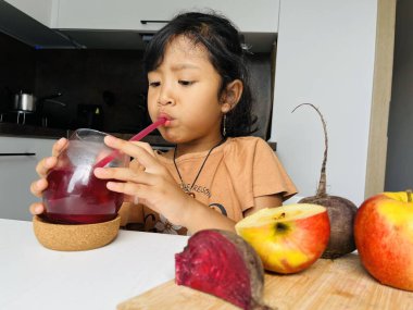 Evdeki mutfakta pancar ve elma suyu içen küçük bir kız. Sağlıklı yeme kavramı.