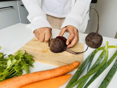 Yemek pişirme konsepti. Beyaz elbiseli, sağlıklı yemek hazırlayan, evde lezzetli yemekler hazırlayan, pancarlı sebzeleri doğrayan, mutfak içini kapatan, tanınmamış bir kadın.