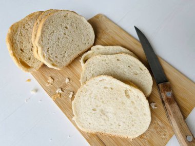 Bir somun ekmek. Kesme tahtasında dilimlenmiş ekmek ve beyaz bir arka planda bıçak.