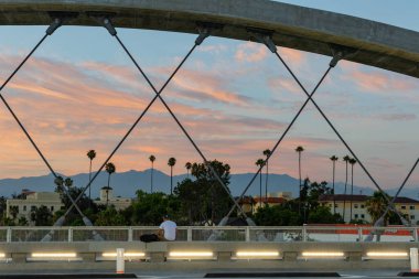 Gün batımı ve palmiye ağaçları Los Angeles 'taki 6. Cadde Köprüsü' nün kemerinden görünüyor.