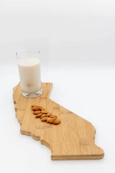 Kaliforniya şekilli kesme tahtasındaki badem sütüyle çevrili bir bardak.