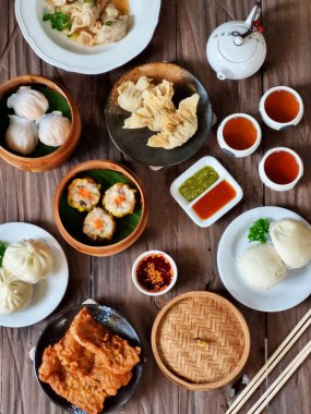 Tahta bir masanın üzerinde çubuk ve çayla donatılmış bambu buharlı bir buharlı Çin Dim Sum 'unun görüntüsü. Asya yemekleri, restoran menüleri ve yemek blogu içeriğini resmetmek için mükemmel.