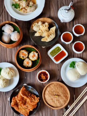 Tahta bir masanın üzerinde çubuk ve çayla donatılmış bambu buharlı bir buharlı Çin Dim Sum 'unun görüntüsü. Asya yemekleri, restoran menüleri ve yemek blogu içeriğini resmetmek için mükemmel.