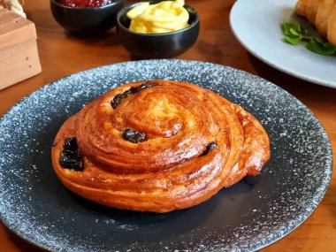 Birkaç taze kruvasan seramik tabakta, bir fincan kahvenin yanında, küçük bir kavanoz krema ve reçel. Bu resim kafe menüleri, yemek blogları, yaşam tarzı dergileri ve aşçılık siteleri için uygundur..