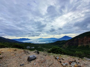 Güneşin doğuşunda Papandayan Dağı 'ndaki Tebing Soni' de Cikuray Dağı ve arkada Guntur Dağı ile sıcak bir atmosfer. Papandayan Dağı, Garut, Batı Java, Endonezya 'da yürüyüş için en sevilen yerlerden biridir..