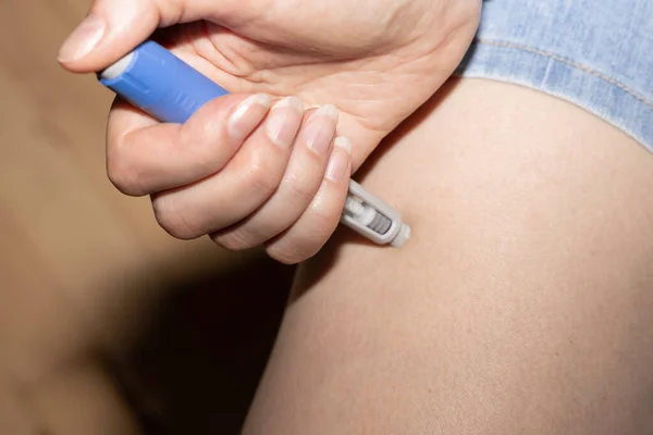 A woman injects insulin into her leg. Insulin injection pen or insulin cartridge pen for diabetics. Medical equipment for diabetes parients.