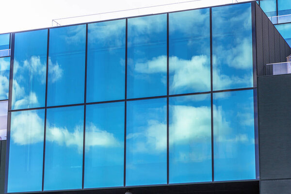 Modern glass building with blue sky and clouds reflection.