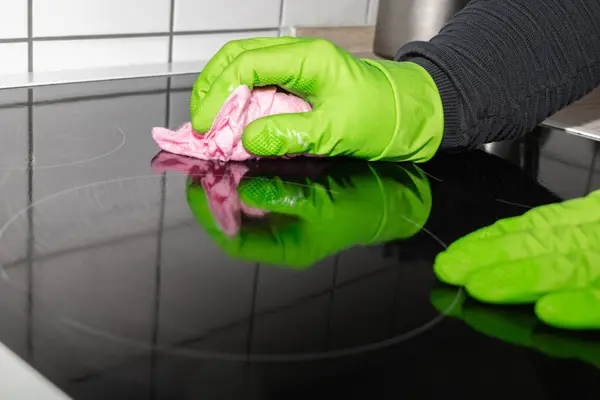 A person in rubber gloves cleaning the induction hob and using cloth and disinfectant spray, detergent. House cleaning and hygiene concept.