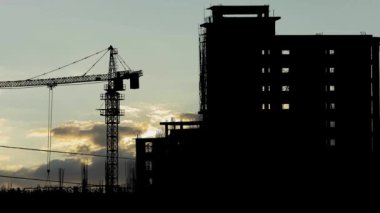 Siluet 'te Büyük Kule Turna ile inşaat alanı, Güneş gittikçe alçalır, manzarada uzun gölgeler bırakır.