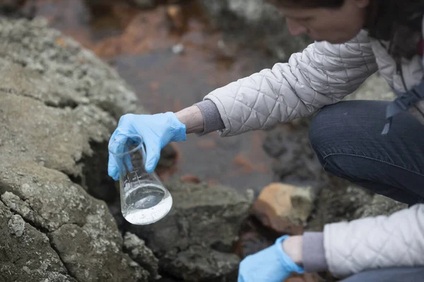 場所の近くで水のサンプルを調べるために 円錐フラスコ化学ガラスウェアを使用する生物学者 — ストック写真