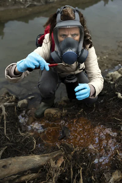 リバーベッドから毒性のサンプルを取るガスマスク付き生物学者 — ストック写真