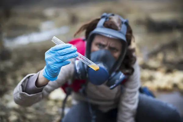 大人の女性生物学者は保護バイオ危険Maskの場所の屋外の汚染された土そして水のテスト管のサンプルを検査します — ストック写真