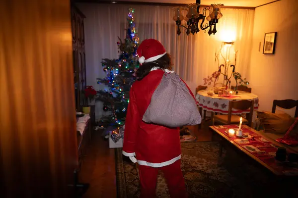 Embracing the Spirit of Christmas, a Single Mother Steps into a Festive Living Room, Dressed as Santa, Carrying a Sack Full of Presents Over Her Shoulder. Ready to Create Joyful Memories in the Traditional Holiday Ambiance