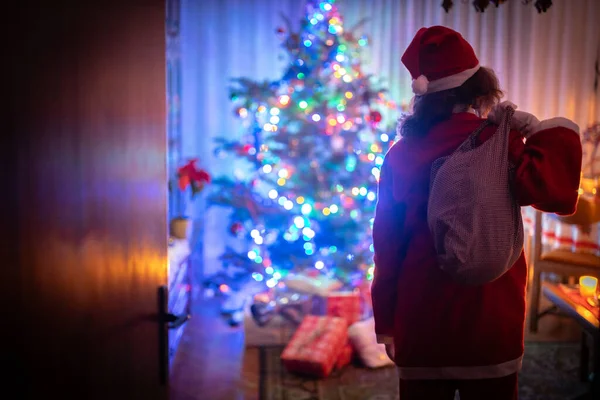 Embracing the Spirit of Christmas, a Single Mother Steps into a Festive Living Room, Dressed as Santa, Carrying a Sack Full of Presents Over Her Shoulder. Ready to Create Joyful Memories in the Traditional Holiday Ambiance
