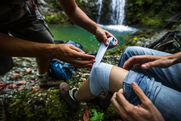 Assistance of a Woman Thigh With an Elastic Medical Bandage from First Aid Travel Kit on a Hike in Wilderness