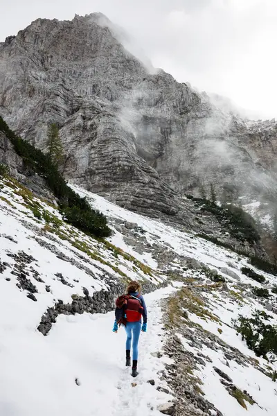 Adventurous Woman Solo Hiking Uphill on a High Mountain Trail Path in Unstable Cold Weather Conditions