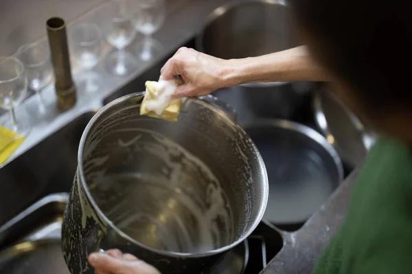 Adult Woman Washes Cooking Pots by Hand in a Restaurant Kitchen Close Up Over the Shoulder View