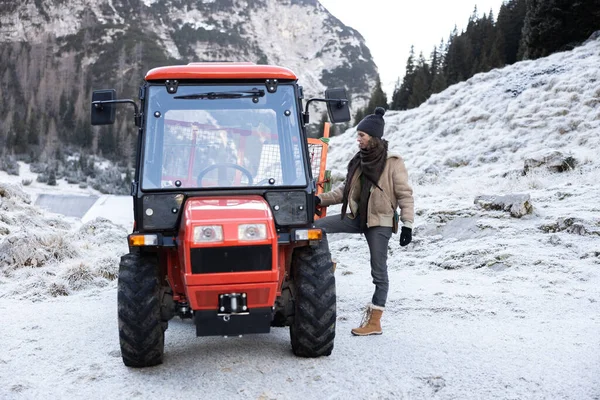 Adult Woman Farmer Getting in a 4x4 Tractor in Winter Rural Frosty Mountain Landscape