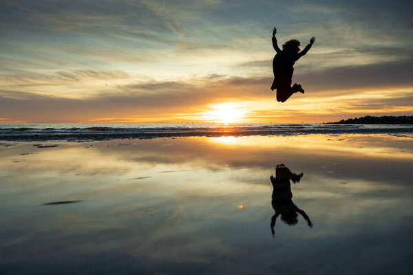 Jumping Curly Hair Woman Silhouette in Mid Air Against Sunset on a Empty Beach