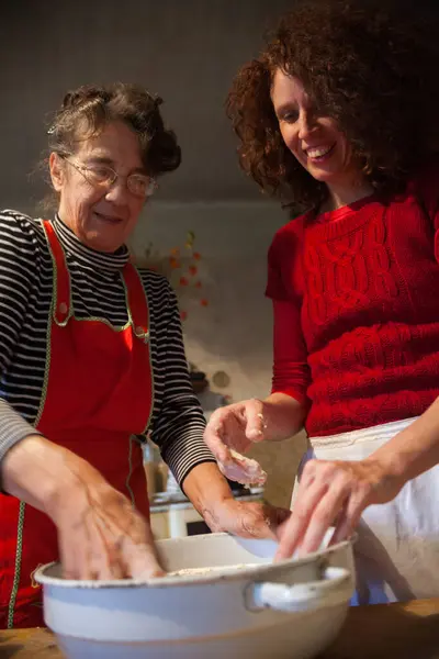 Expert Senior Woman Baker Enjoying teaching A Smiling Adult Woman the Art of Hand Making Bread Dough