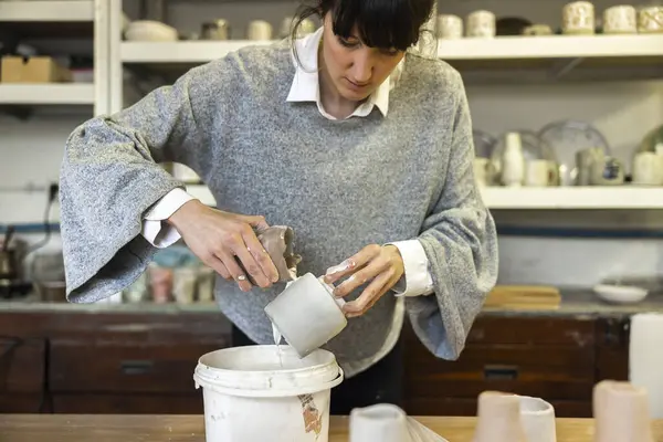 Ceramic Artist putting finish ceramic glaze on a crafted cup in her studio workshop