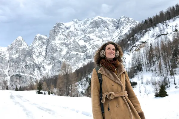 In the Serene Embrace of a Snowy Mountain Landscape, a Vintage Dressed Adult Woman Radiates Positivity and Joy While on a Healthy Walk on Snow. Her Smile Mirrors the Tranquility of Surrounding Breathtaking Environment
