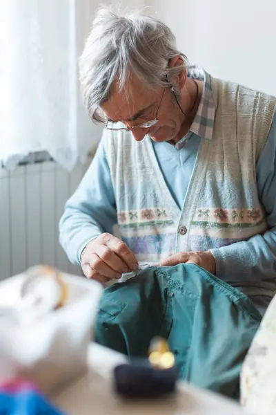 Senior Man Sewing His Jacket Strap at Home By Hand