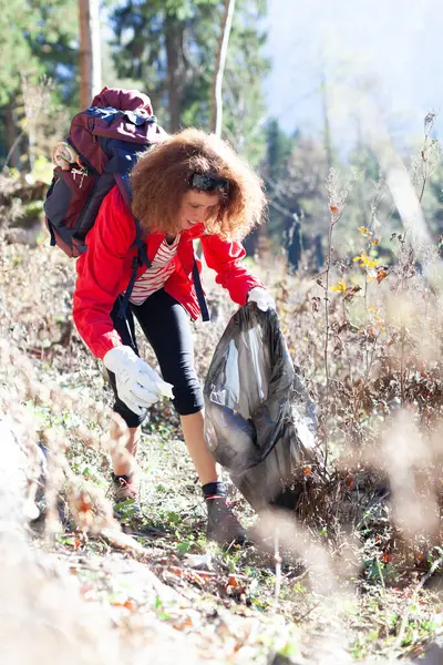 Woman Backpacker Ecologist Collecting Trash From Nature of Mountain Environment and put it into a Garbage Bag