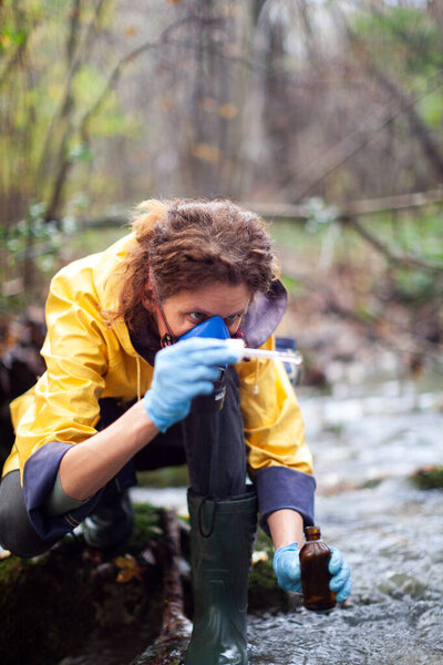 Concentrated Caucasian Female Environmental Biologist Collecting Samples of Water for Further Examination from a Water Stream