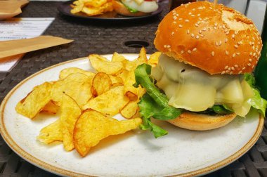 Eritilmiş peynirli leziz bir çizburger, kızarmış patates kızartması ve kırsal beyaz tabak arka planında taze marul yemek atmosferini geliştirir. Anın tadını çıkar.!